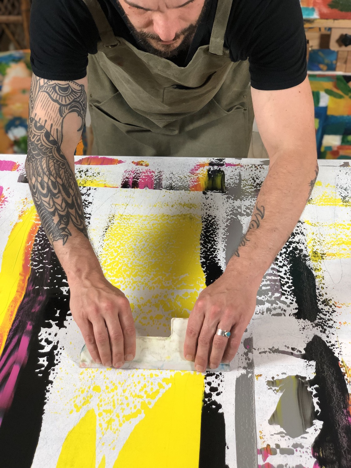 Dylan Yarter pulling a scraper across thick yellow and black paint on a canvas